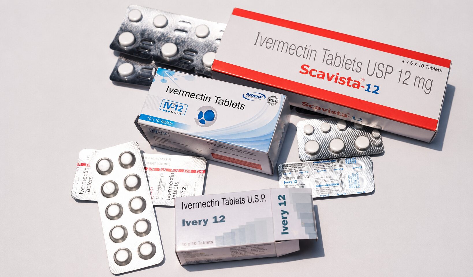 Assorted ivermectin tablet boxes and blister packs arranged on a light surface, showing Scavista-12 and Ivermetin packaging with capsules visible in blisters