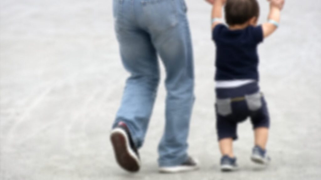 Adult and child walking away together on a light pavement surface.