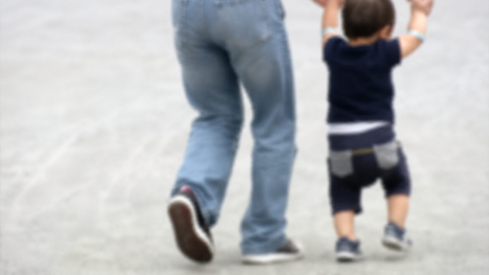 Adult and child walking away together on a light pavement surface.