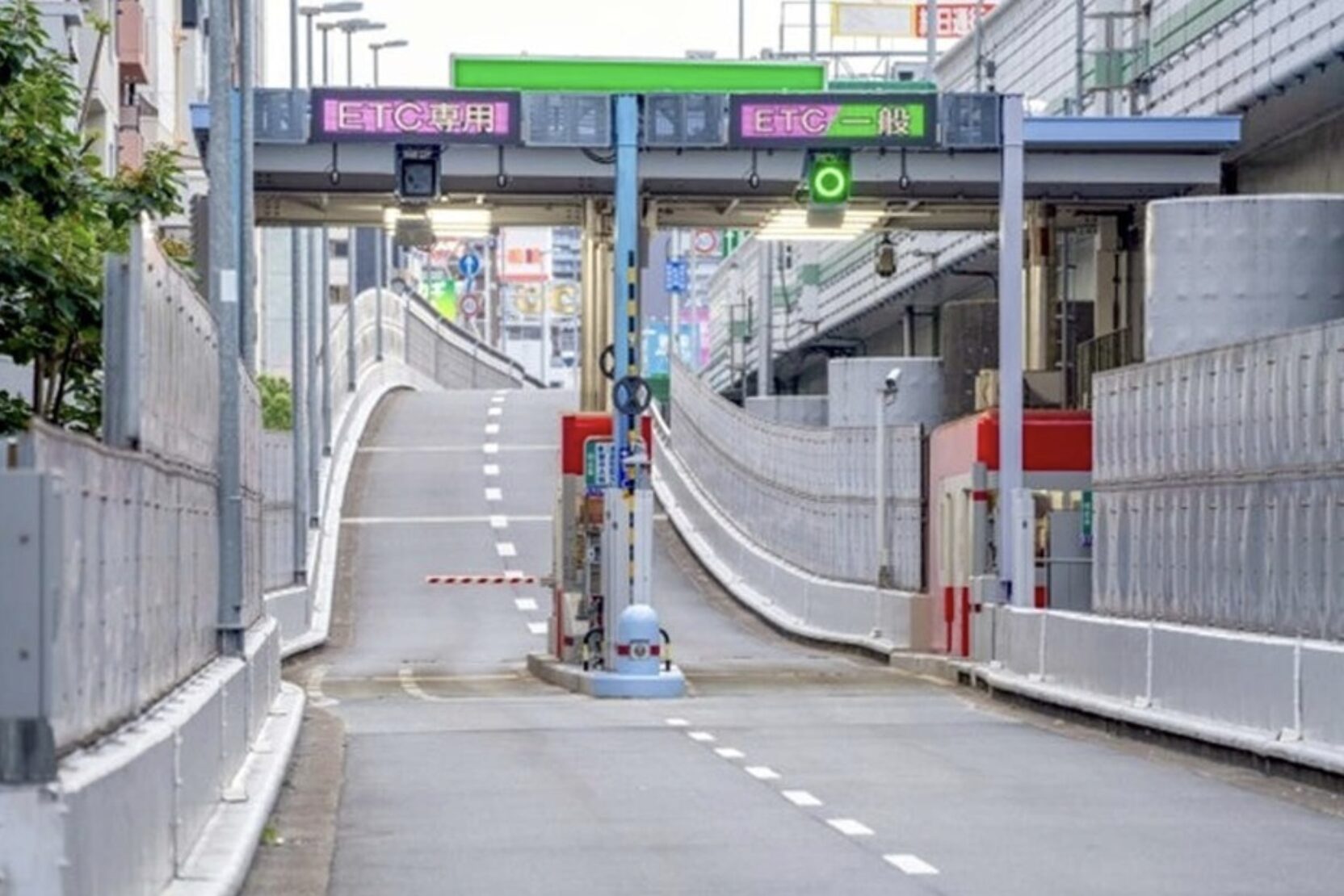 Entrance to a sunken city road with a curved ramp, concrete barriers, and metal fencing; overhead signage visible in urban setting.