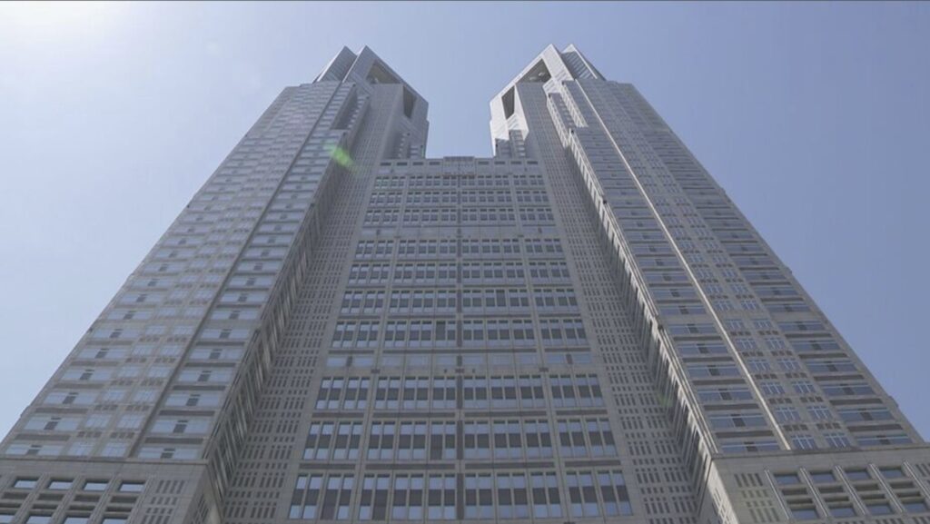 Low-angle view of a pair of tall modern skyscrapers connected by a central podium against a clear blue sky.