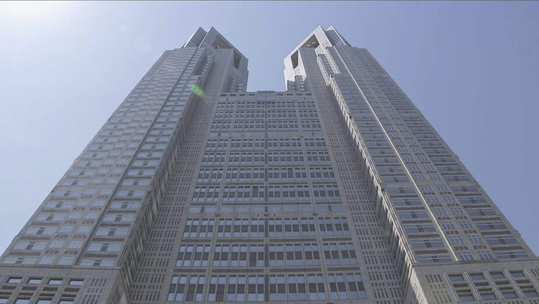 Screenshot - Empregos no Japão Low-angle view of a pair of tall modern skyscrapers connected by a central podium against a clear blue sky.