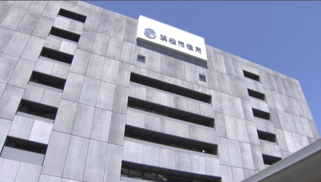 Modern gray concrete office building with a white sign and blue logo at the top, against a clear blue sky