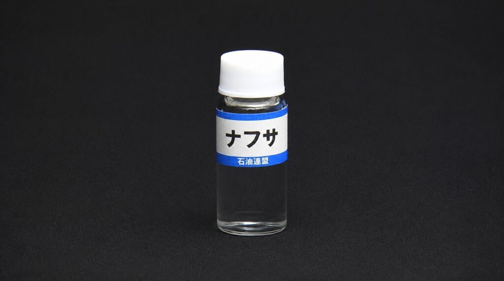 Small clear liquid in a tiny bottle with a white cap, labeled ナフサ (naphtha) in Japanese on a blue-and-white band.