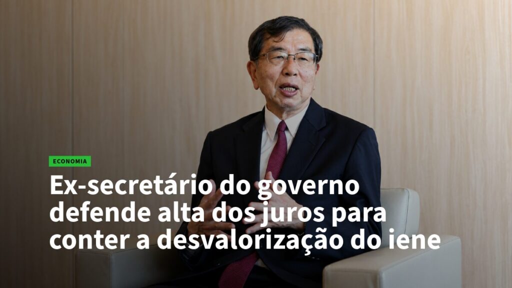 Homem de terno em entrevista, com manchete em português sobre defesa de alta de juros para conter a desvalorização do iene.