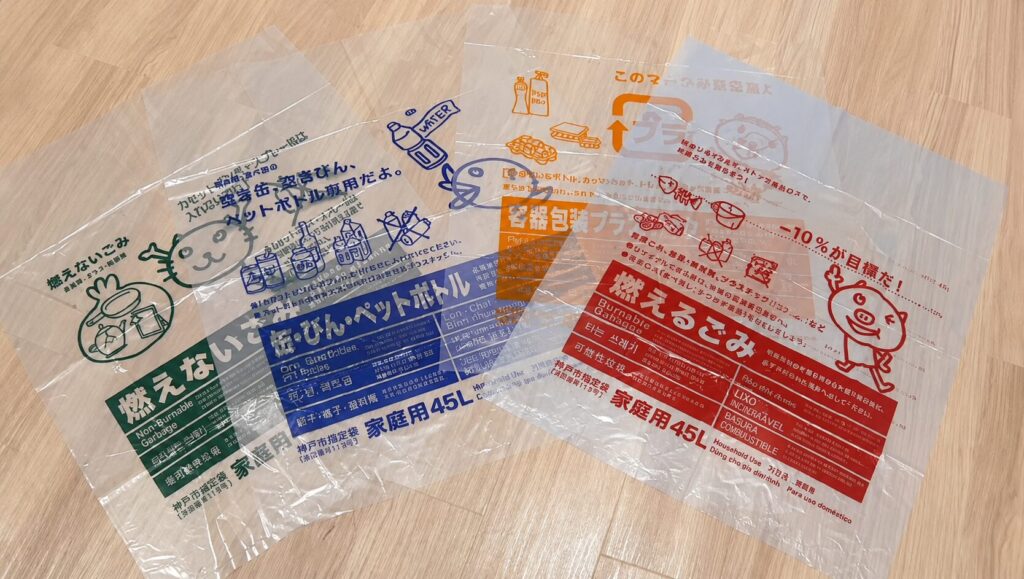 Transparent plastic garbage bags with colorful Japanese recycling labels and cute cartoon characters on a wooden floor.